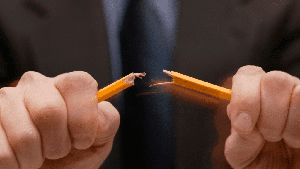 Close-up of a person snapping a pencil in frustration, symbolizing uncontrolled anger.
