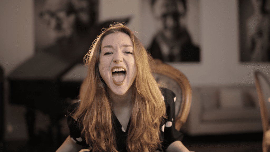 A frustrated woman with long blonde hair yelling in an indoor setting, representing uncontrolled emotional outbursts and needing ways for managing anger.