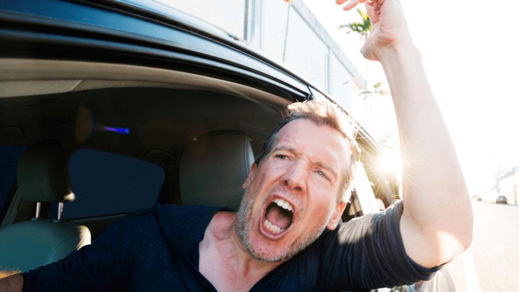 A frustrated man yelling out of a car window, illustrating road rage and reactive anger.

