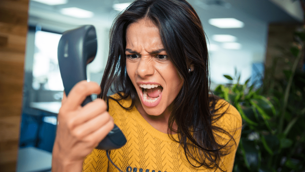 A woman in an office setting yelling into a phone, showing frustration in workplace interactions.
