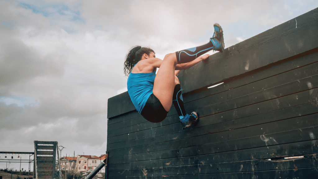 A determined woman climbs over a large obstacle wall, illustrating the resilience needed for overcoming obstacles in leadership.
