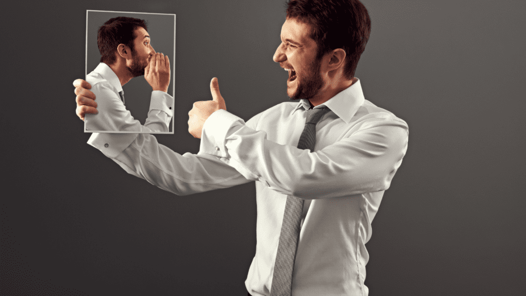 A businessman speaks to his reflection, symbolizing the internal battle leaders face in overcoming obstacles in leadership.

