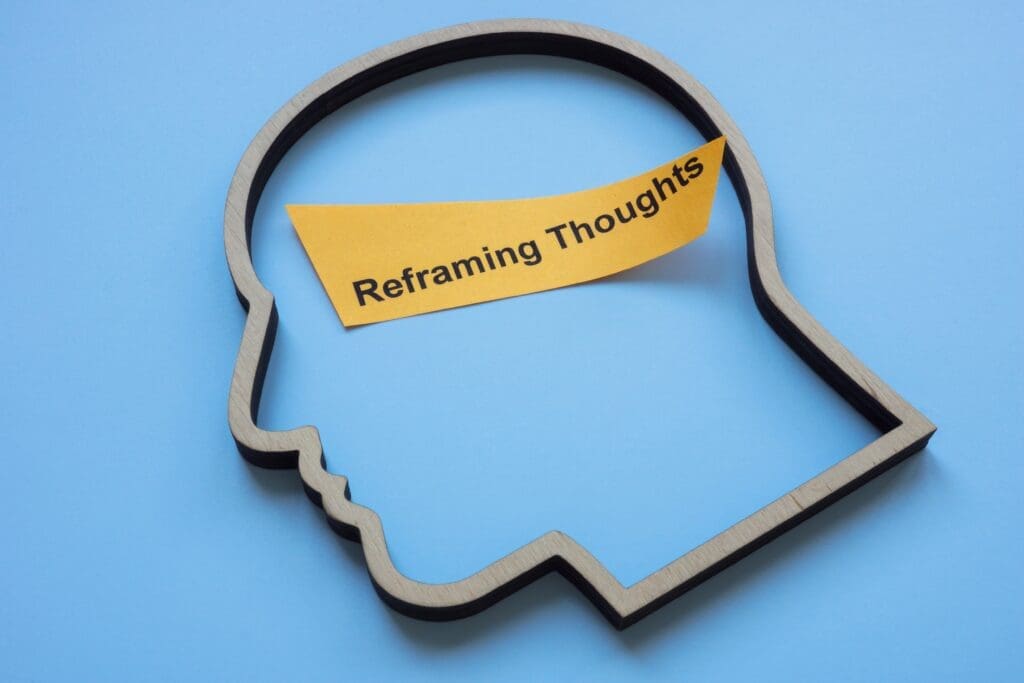 A wooden outline of a human head with a note reading "Reframing Thoughts," symbolizing cognitive restructuring techniques.