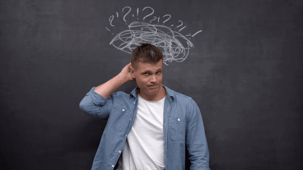 Man standing in front of a chalkboard with question marks, depicting uncertainty in the neuroscience of insecurity



