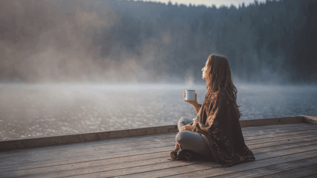 Person sitting peacefully by a lake with a cup, embodying the calm and clarity achieved through digital detox.





