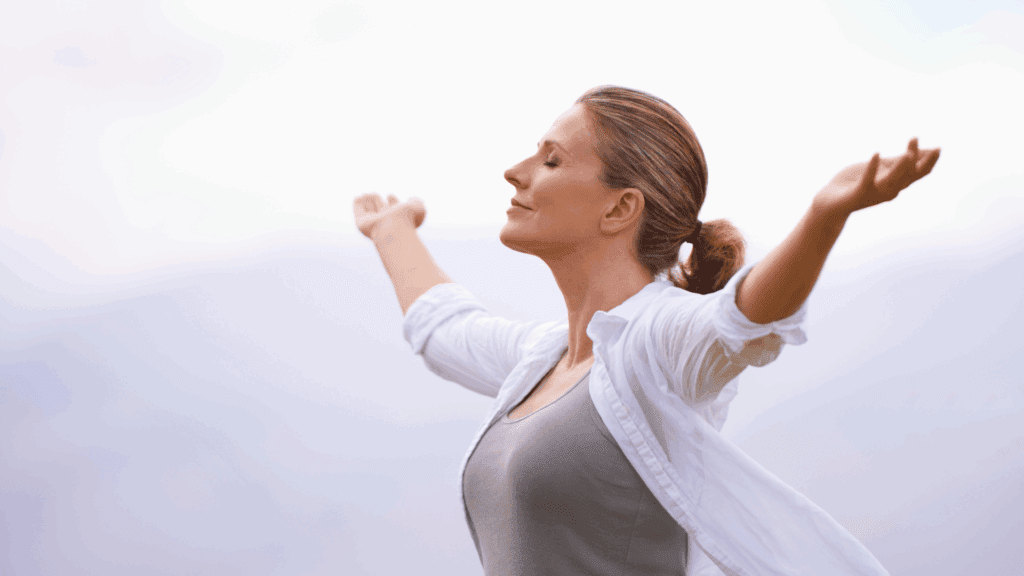 A woman standing outdoors with arms raised in a gesture of vitality, representing the benefits of dopamine boosting foods.