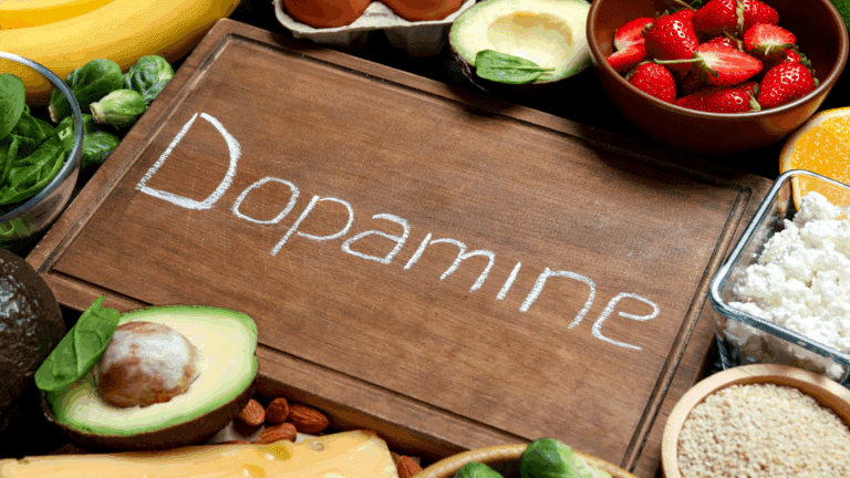 On the Blog 4 A selection of dopamine boosting foods including avocado, strawberries, eggs, spinach, and cheese arranged around a wooden board with Dopamine written on it.