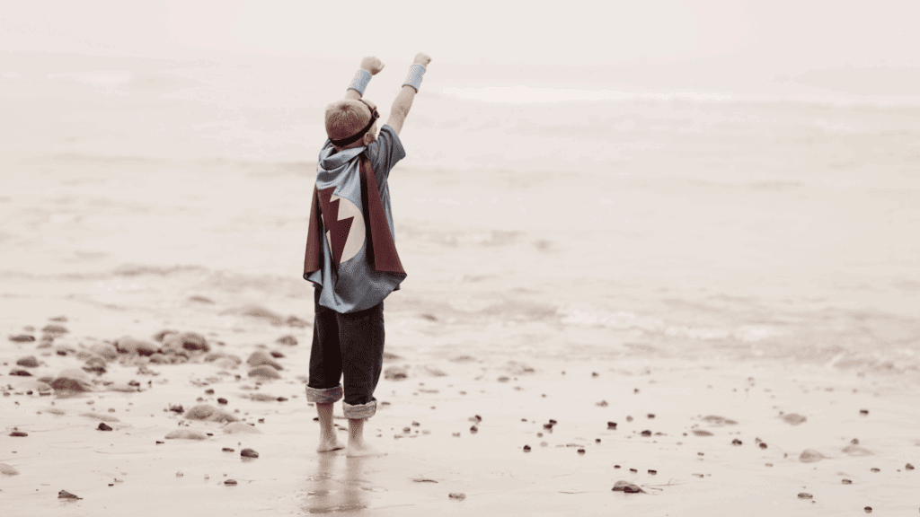 Child in a superhero cape standing on a beach, symbolizing executive presence and confidence.

.



