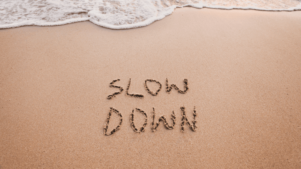 The words “slow down” written in the sand near gentle ocean waves, representing mindfulness of anxiety.



