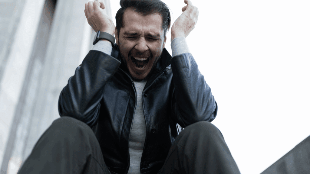 A person sitting outdoors with their head in their hands, showing a moment of stress and reflection on mindfulness of anxiety.