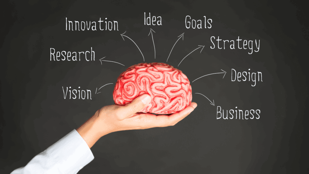 Hand holding a model brain with arrows showing goals and strategy in neuroplasticity coaching.