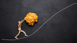 Wooden figure pushing a yellow ball uphill, illustrating perseverance in the neuroscience of mental toughness.