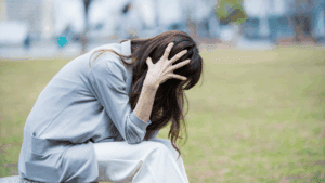 Woman sitting outdoors holding her head in distress, illustrating symptoms of anxious depression.