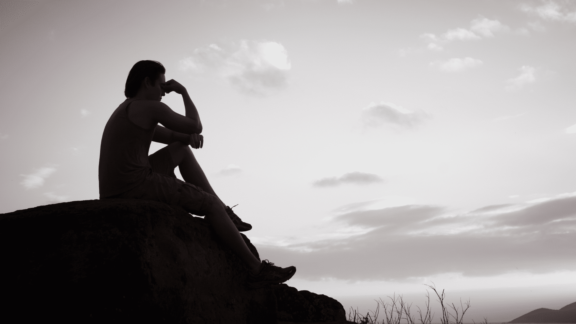 Man sitting alone on a rock at sunset, symbolizing feelings of isolation and fear of being alone linked to autophobic thoughts.