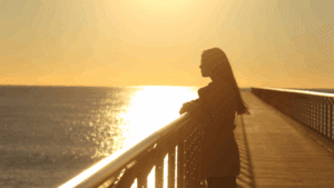 Woman standing alone on a pier at sunset, symbolizing autophobic struggles with solitude and self-reflection.