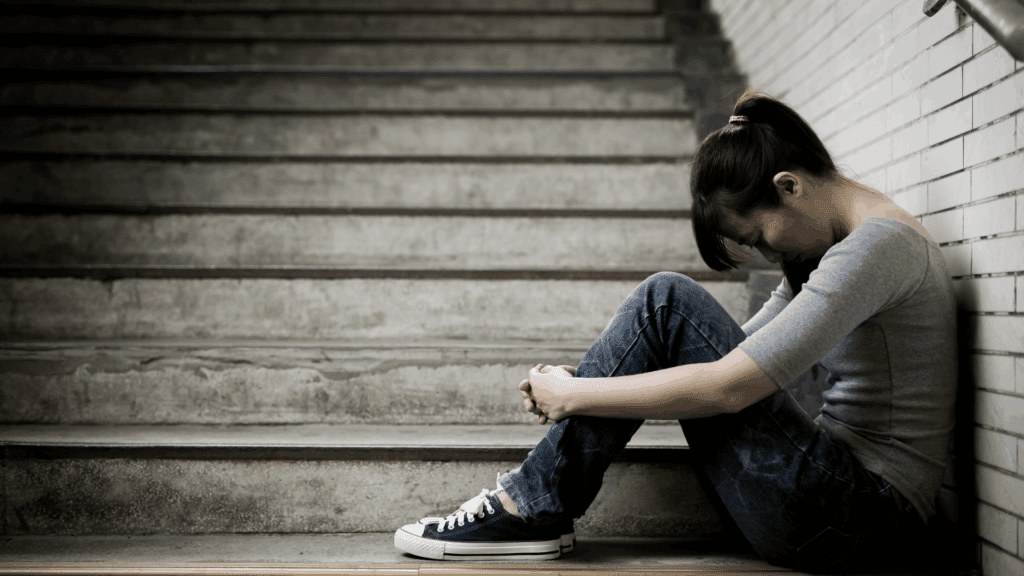 Young woman sitting on stairs with her head down, showing emotional distress linked to dopamine depletion.