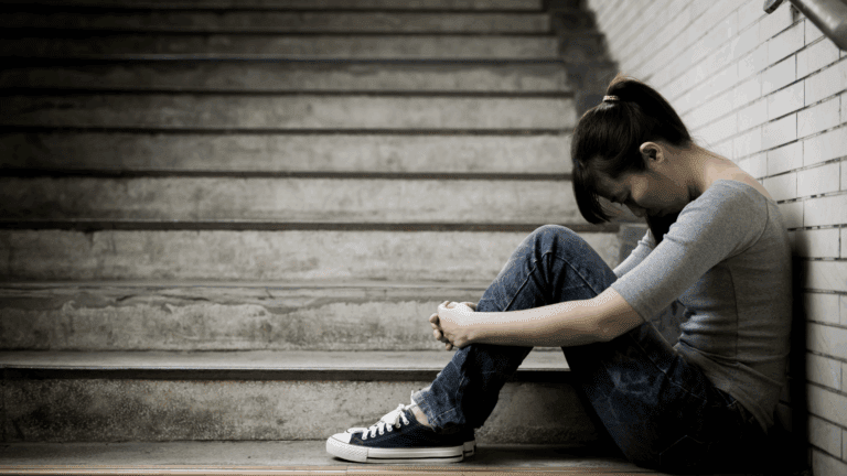 Young woman sitting on stairs with her head down, showing emotional distress linked to dopamine depletion.