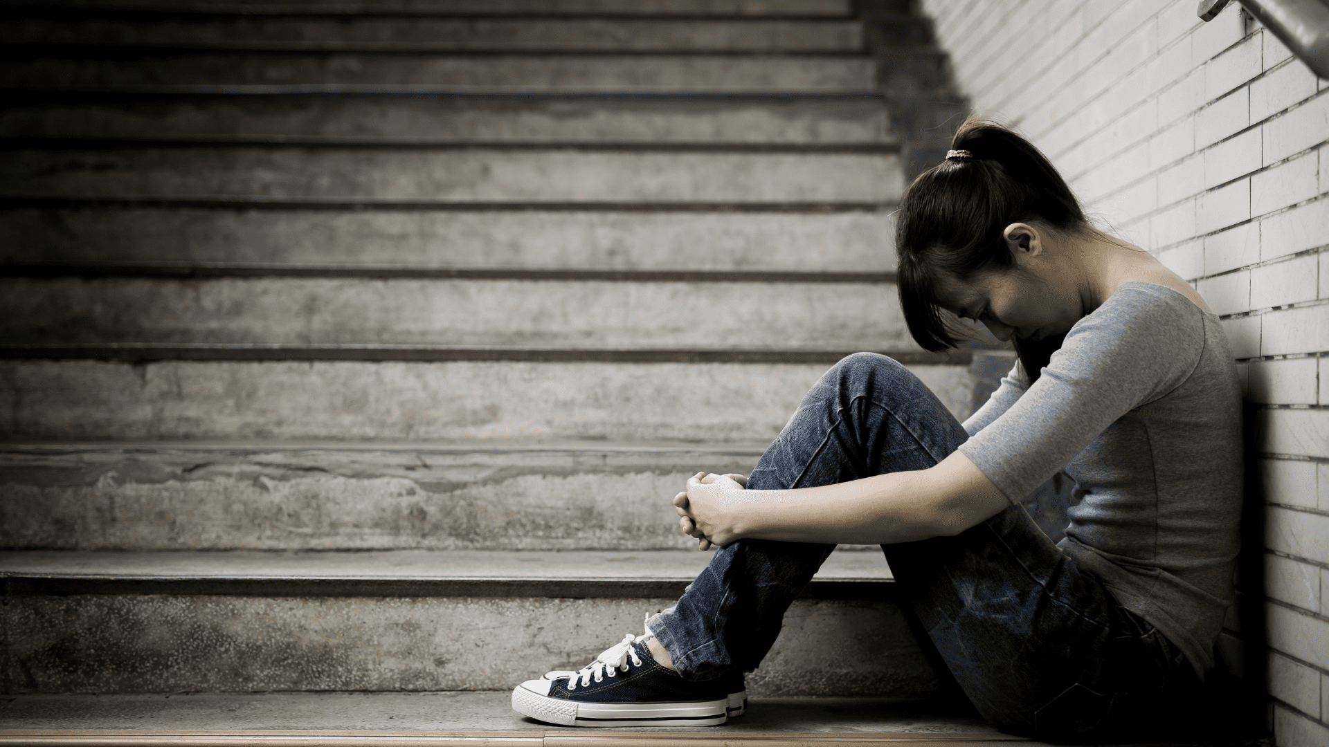 Young woman sitting on stairs with her head down, showing emotional distress linked to dopamine depletion.
