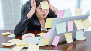 Stressed woman surrounded by sticky notes at her desk, highlighting challenges that impact leadership presence.