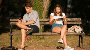 Hooked on YouTube Shorts: How Reward Loops Hijack Your Brain 1 Couple sitting on a park bench distracted by phones, illustrating reward loops in digital behavior.