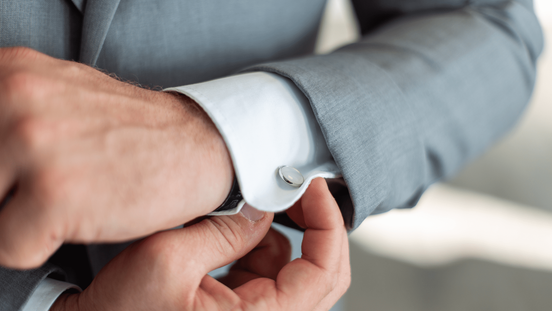 Man adjusting cufflinks on a suit sleeve, symbolizing confidence and refinement tied to alpha vs beta traits.