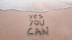 “Motivational words ‘Yes you can’ written in sand by the ocean, symbolizing optimism and the power of Dopamine Coaching Neuroscience.”