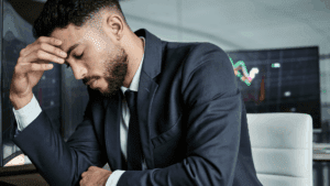 Frustrated businessman sitting at desk with hand on forehead, illustrating the stress and frustration of feeling stuck at work.