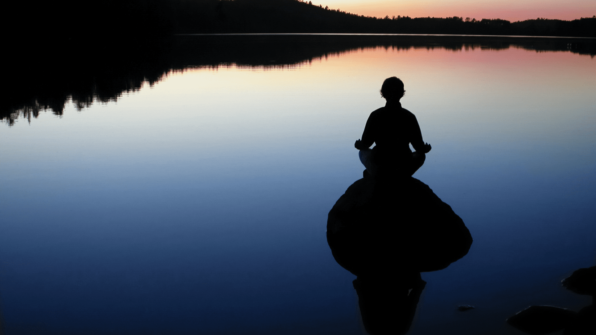 Person meditating by a calm lake at sunset, symbolizing mindfulness and neuroplasticity through peaceful awareness.