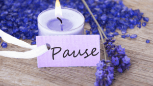Mindfulness and Neuroplasticity: How to Rewire Your Brain for Calm and Confidence 1 Lit lavender candle with purple flowers and a note reading “Pause,” symbolizing mindfulness and neuroplasticity through relaxation.