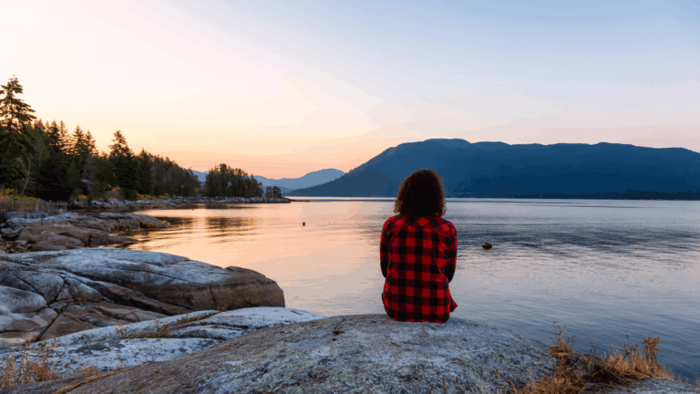 Person sitting by a calm lake at sunset, symbolizing peace and mindfulness through neuroscience-based anxiety relief.