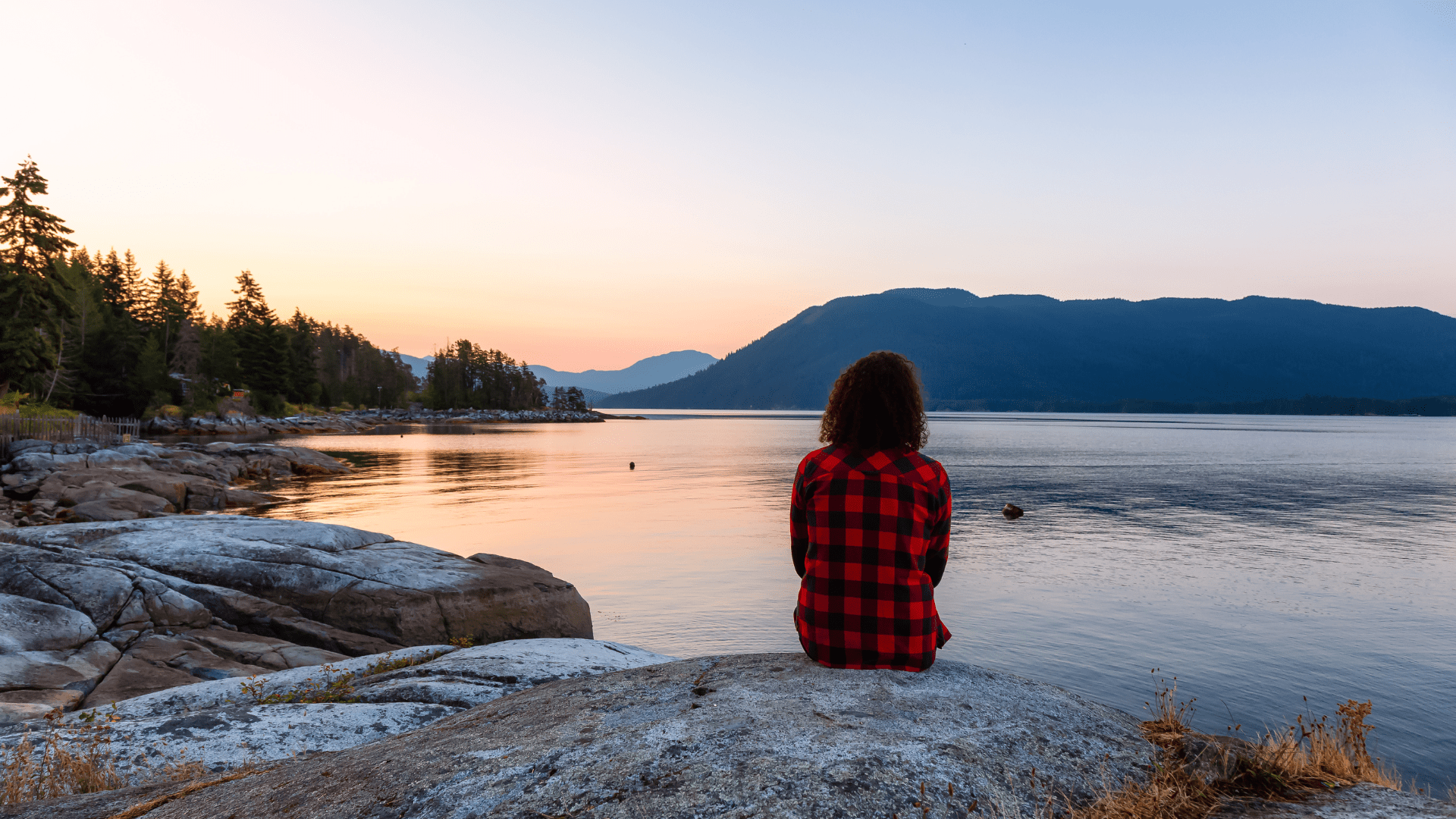 Person sitting by a calm lake at sunset, symbolizing peace and mindfulness through neuroscience-based anxiety relief.