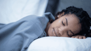 Woman peacefully napping under a gray blanket, illustrating rest and recovery emphasized in virtual wellness coaching tips.