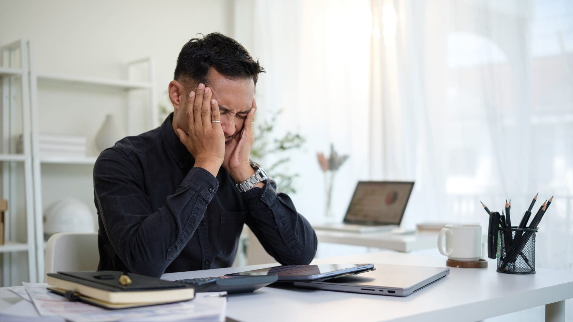 Stressed man holding his head in his hands at a desk, symbolizing anxiety and overthinking linked to what if thinking.
