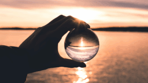 Hand holding a glass sphere reflecting a sunset, symbolizing the illusion and allure behind why we want what we can't have.
