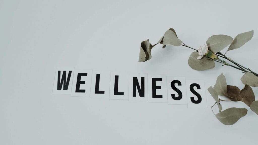 Wellness text spelled out on white tiles with fresh eucalyptus branch, representing holistic dopamine mental health and well-being achieved through neuroscience-based lifestyle optimization.