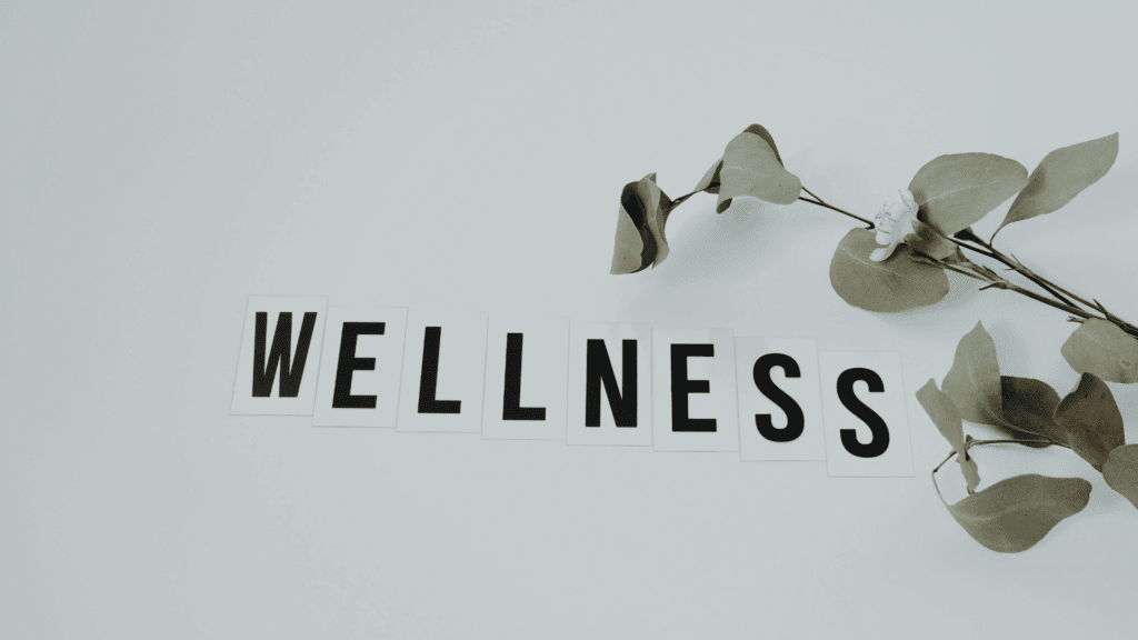 Wellness text spelled out on white tiles with fresh eucalyptus branch, representing holistic dopamine mental health and well-being achieved through neuroscience-based lifestyle optimization.
