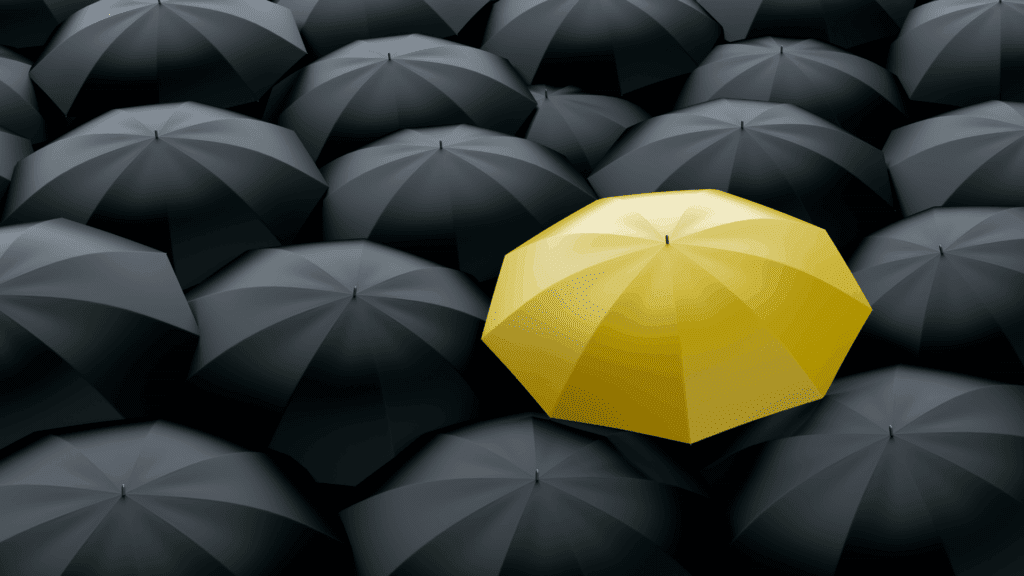 Life Coaching vs Neuroscience Coaching: A Complete Guide 3 Yellow umbrella standing out among black umbrellas symbolizing differentiation in life coaching vs neuroscience coaching