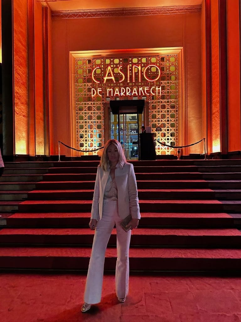 Dr. Sydney Ceruto 51 Dr. Sydney Ceruto in an elegant white suit standing on the grand red-carpeted steps of Casino De Marrakech at night