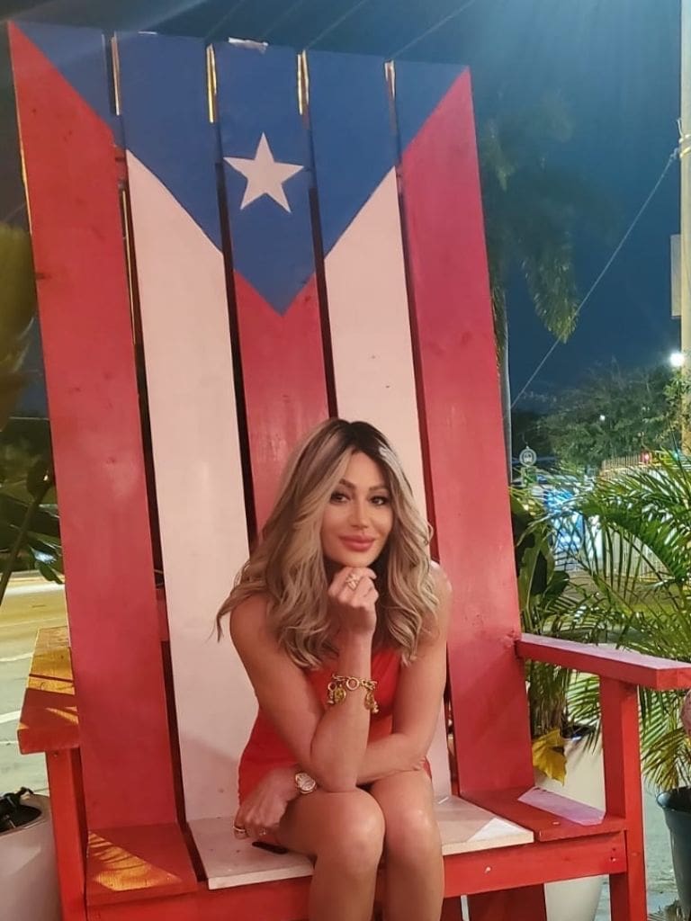 Dr. Sydney Ceruto 46 Dr. Sydney Ceruto smiling in a red dress seated on an oversized Puerto Rican flag chair during a night out in Puerto Rico